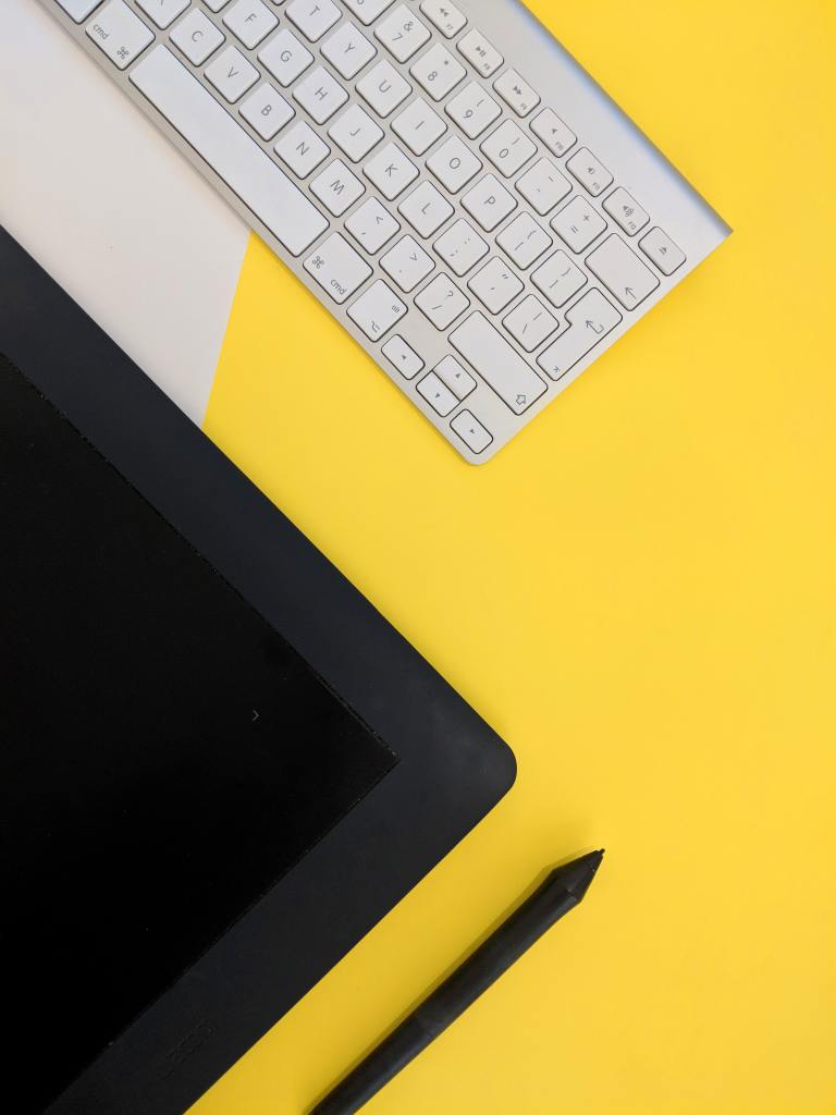 Keyboard, drawing tablet and pen on a yellow background.
